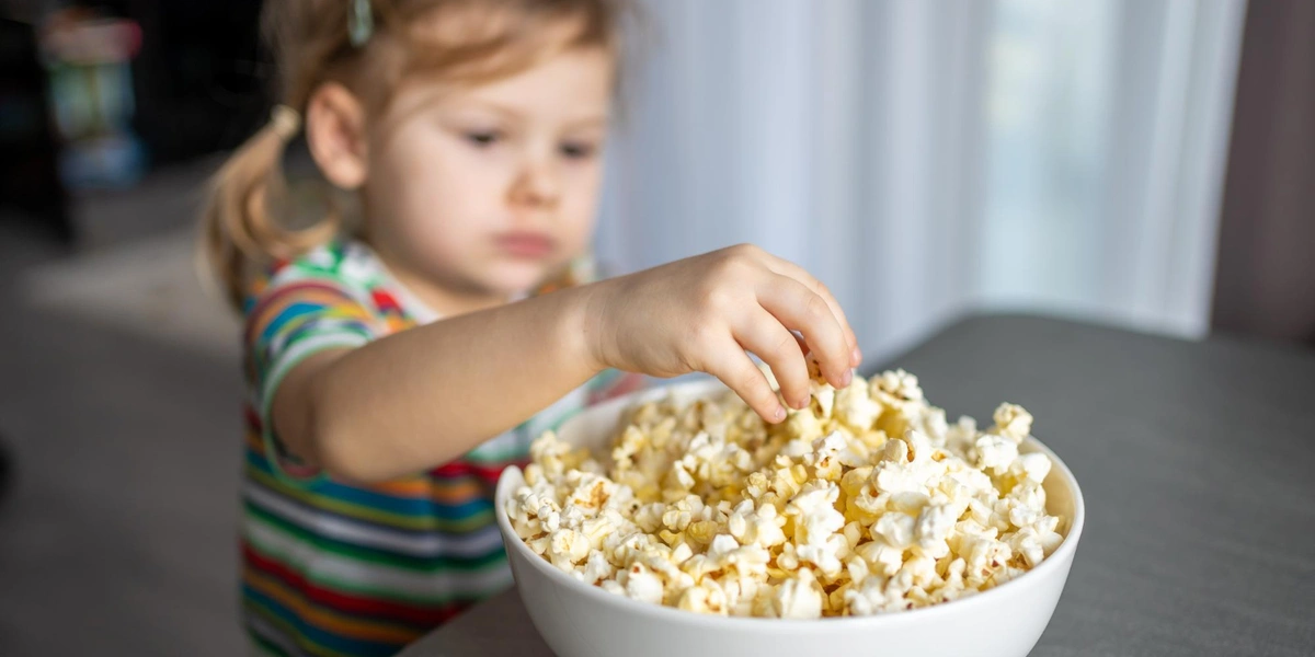 Dziecko wyciąga popcorn z miski