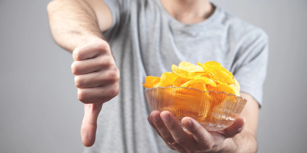 Męzczyzna trzyma miskę chipsów i pokazuje kciuk w dół